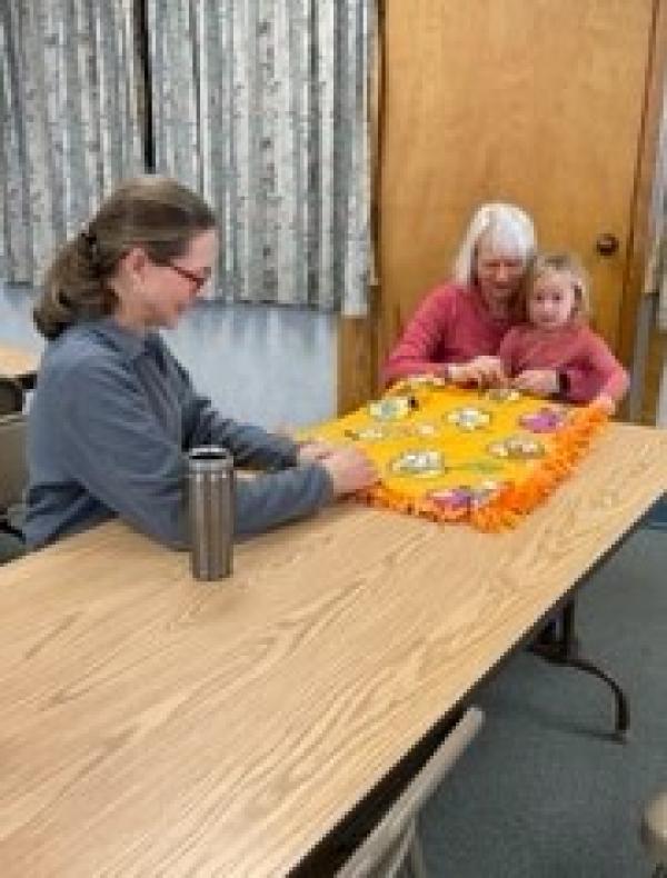 Pat Lemay and her granddaughter work with Jean Clary to tie one of the prayer blankets